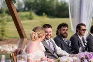 Wedding party sharing a laugh at the head table during outdoor reception.