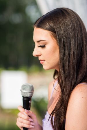 Close-up profile view of someone speaking into a microphone during an outdoor event.