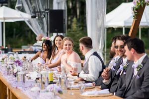 Wedding reception guests seated at long tables under white tent with elegant decor.