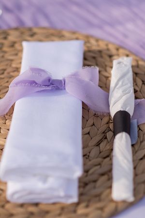 White napkins with lavender ribbons arranged on woven charger plates.
