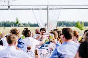 Wedding reception dinner under white tent with guests seated at decorated tables.