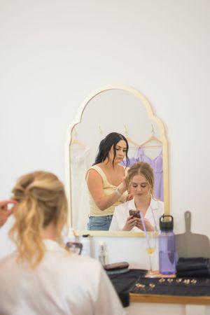 Wedding preparation scene with stylists working on hair and makeup in front of vintage mirrors.