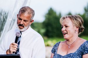Wedding speeches and toasts being given during outdoor reception under clear tent.