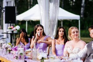 Wedding reception tables decorated with purple floral centerpieces and white linens under an outdoor tent.