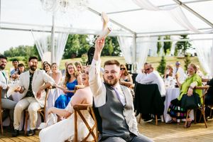 Wedding celebration in white tent with guests enjoying festivities at decorated tables.