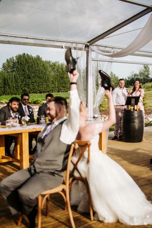 Wedding celebration under white tent with guests seated at wooden tables.