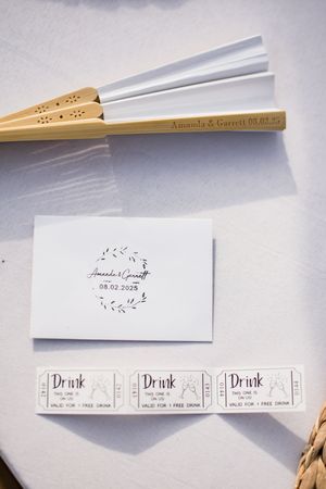 Wedding favor fans with drink tickets and decorative details laid out on white background.