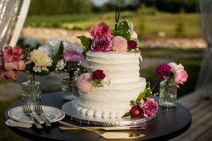 White wedding cake decorated with fresh pink and burgundy flowers on dark display stand.
