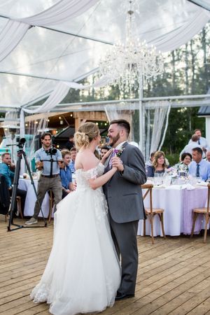 First dance sequence under white tent with crystal chandeliers and reception tables.