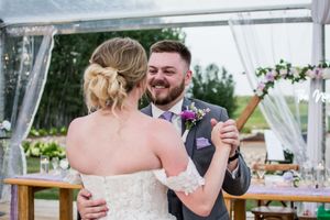 Guests celebrate at an elegant outdoor wedding reception under white tent draping.