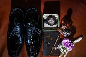 A collection of black leather shoes and boots arranged in a row with purple flowers and accessories.