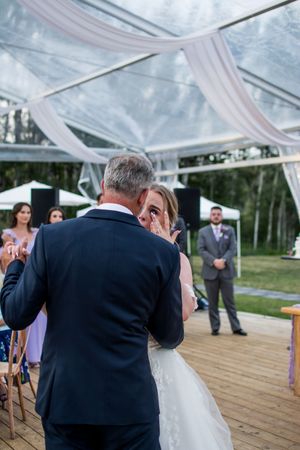 Wedding ceremony moments captured under a clear tent with white fabric draping and wooden deck flooring.