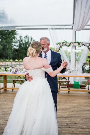 A tender dance moment between a bride in white and an older gentleman at an outdoor wedding reception.