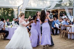 Outdoor wedding reception under white tent with purple decor and string lights.