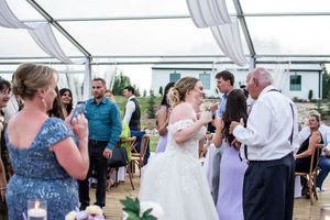 Wedding reception celebration under a white tent with guests dancing and mingling.
