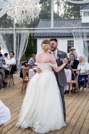 Wedding reception dance floor with white tent, sheer curtains and crystal chandeliers overhead.