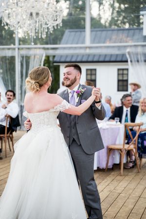 Wedding couple shares first dance under crystal chandelier on wooden deck.