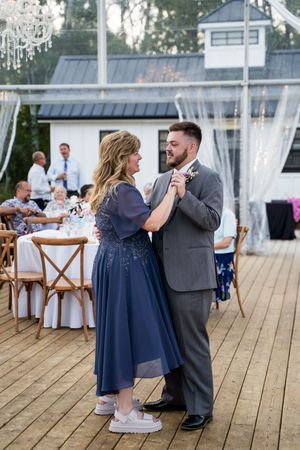 Couples dancing on a wooden deck under an elegant white tent with chandeliers and sheer drapes.