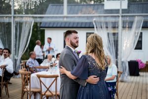 Outdoor wedding reception venue with white drapes and cross-back chairs on a wooden deck.