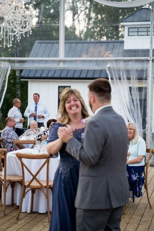 Wedding guests dancing and celebrating on an elegant outdoor deck with sheer white curtains.