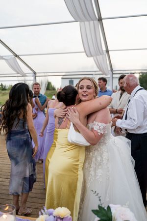Wedding celebration with guests in colorful dresses embracing under a white tent reception.