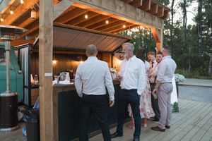 Evening wedding reception on wooden deck with string lights and rustic beams.
