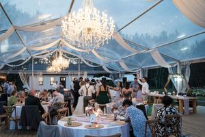 Evening wedding reception in a clear tent with crystal chandeliers and elegant white draping.