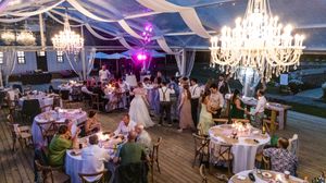 Elegant wedding reception setup with crystal chandeliers and white draping in an outdoor tent venue.