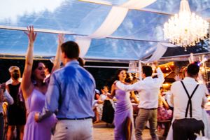 Wedding guests dancing with raised arms during sunset celebration under tent.