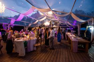 Outdoor wedding reception tent decorated with white drapes and purple lighting creating an elegant evening ambiance.