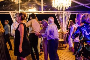 Evening wedding reception with guests dancing under elegant chandeliers and purple lighting.