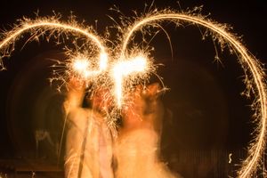Golden sparklers creating light trails and patterns against a dark night sky at a celebration.