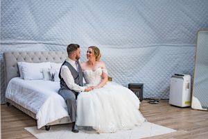 Couple poses on white chaise lounge during elegant wedding photoshoot.