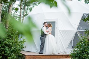 Wedding couple shares romantic moments among lush greenery and white tents during an outdoor celebration.