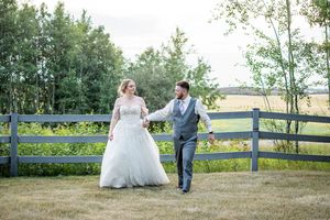 Newlyweds pose for romantic photos along a rustic wooden fence in a countryside setting.