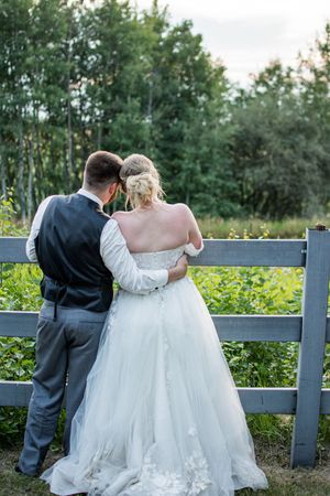 A couple shares an intimate moment while standing against a rustic wooden fence at their outdoor wedding.