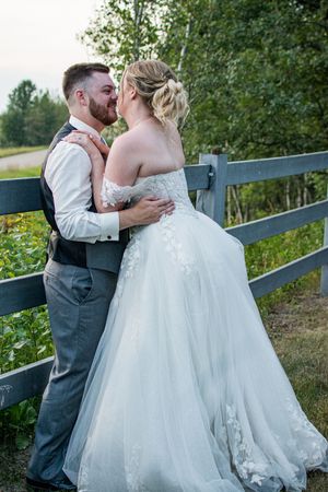 A romantic wedding couple shares an intimate moment along a rustic wooden fence in an outdoor garden setting.