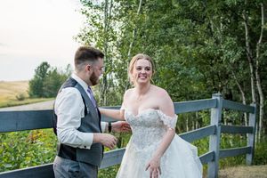 Outdoor wedding photography along a rustic wooden fence with greenery in the background.