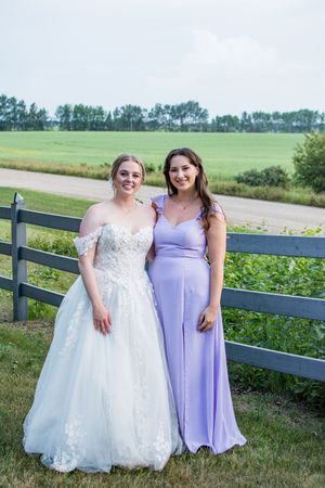 Wedding party in purple and white dresses posing by a wooden fence in a countryside setting.