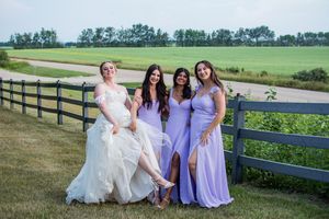 Wedding party in purple dresses and white gown gathered outdoors with scenic countryside views.