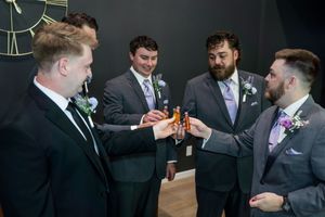 Group of groomsmen in suits toasting with drinks before the wedding ceremony.
