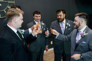 Groomsmen in gray suits sharing drinks and laughs during wedding celebrations.