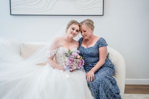 A tender moment shared on a white couch with a beautiful bridal bouquet of purple and pink flowers.