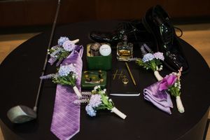 Wedding accessories including purple ties, boutonnieres, and cologne arranged on a black table.