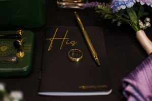 Elegant wedding details including rings and stationery in moody purple lighting.