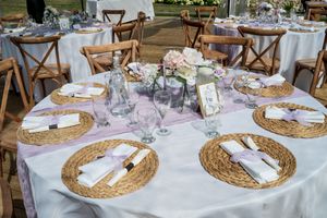 Elegant table setting with woven chargers, purple accents, and floral centerpieces at a wedding reception.