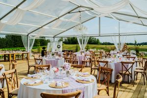 White tent reception setup with round tables and cross-back chairs for wedding celebration.