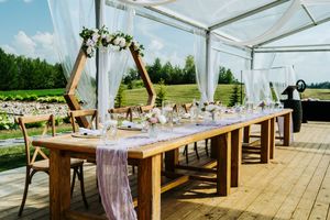 Rustic wedding reception table with wooden chairs and flowing fabric runner under a clear tent.