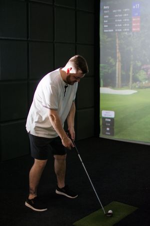 A person practicing their golf swing in an indoor golf simulator with projected screen display.