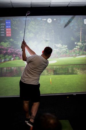 People playing virtual golf on a large projection screen in a dimly lit indoor setting.
